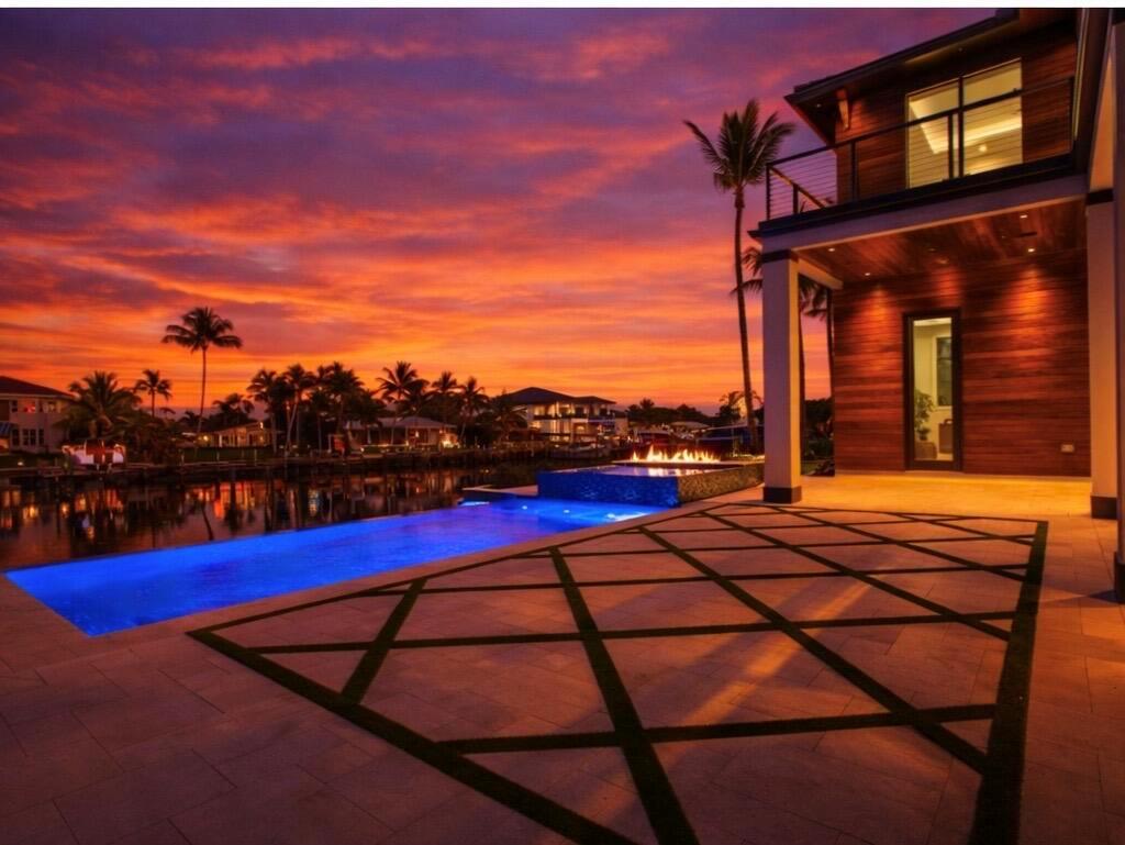 A modern house with a pool and fire feature overlooks a canal at sunset — 736 Lagoon Drive, North Palm Beach FL 33408, NORTH PALM BEACH, FL