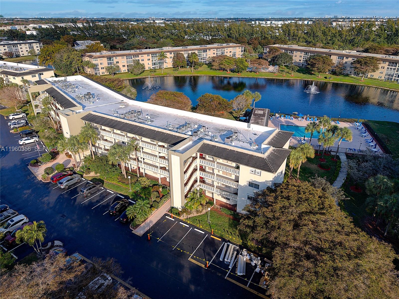 An aerial view shows a multi-story apartment building next to a swimming pool and lake — 1803 Eleuthera Pt # G4, Coconut Creek FL 33066, COCONUT CREEK, FL