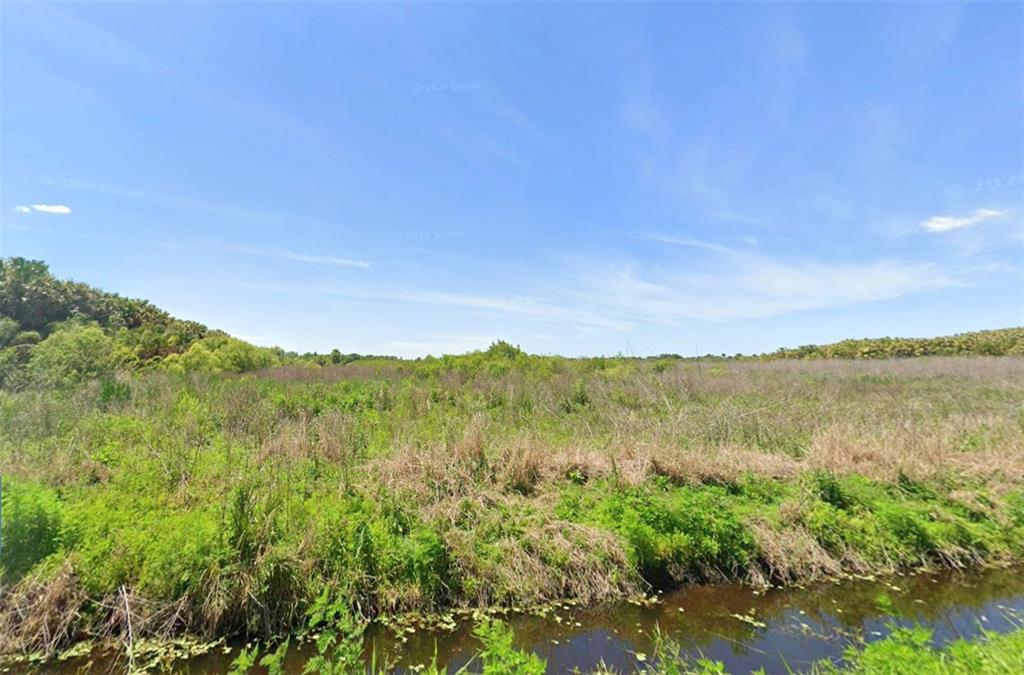 A grassy field with shrubs and trees borders a small canal under a blue sky — 1608 OKLAHOMA STREET, OVIEDO, FL