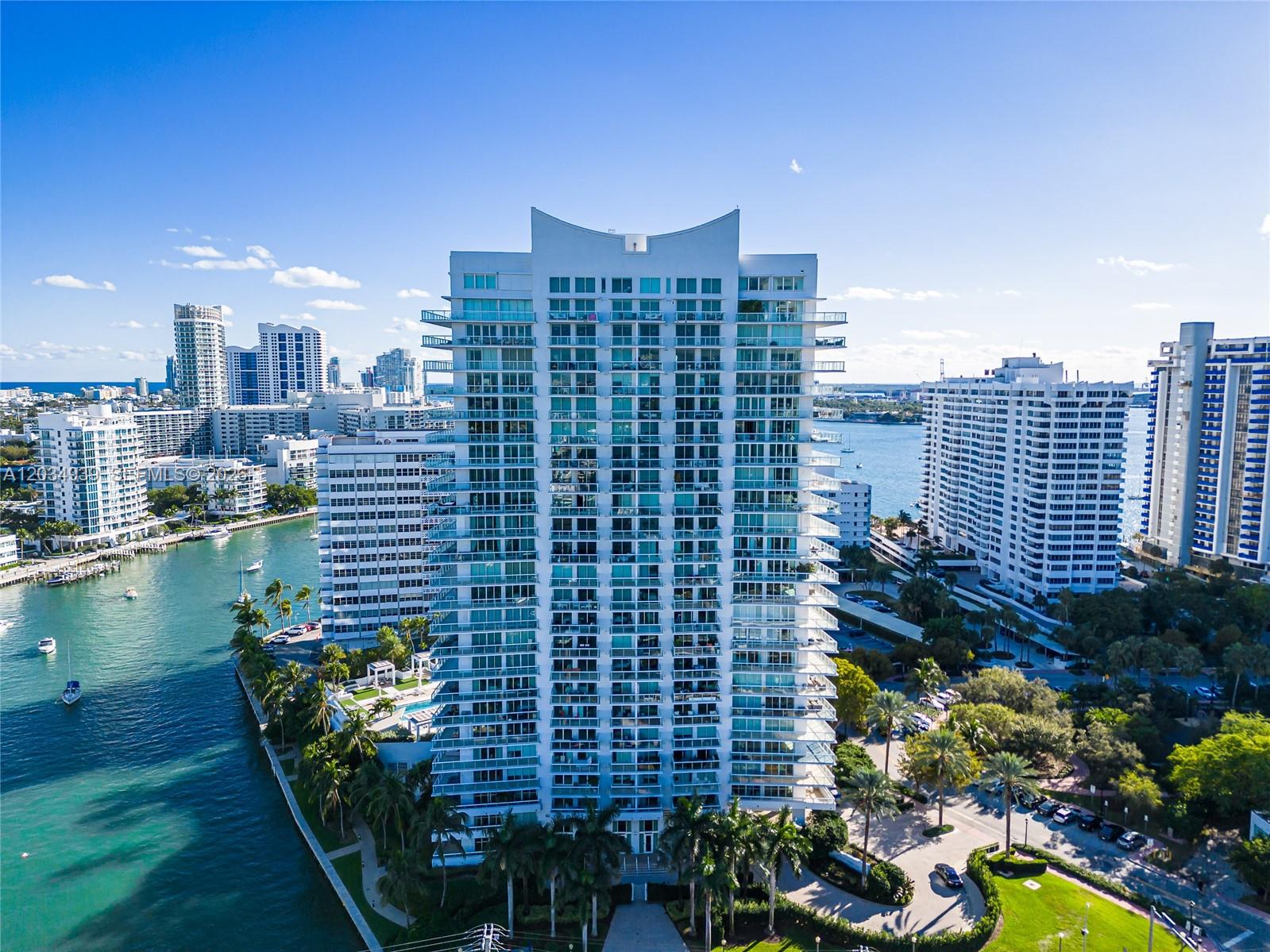 An aerial view of a tall white residential tower surrounded by water and palm trees — 10 Venetian Way, Miami Beach FL 33139, MIAMI BEACH, FL