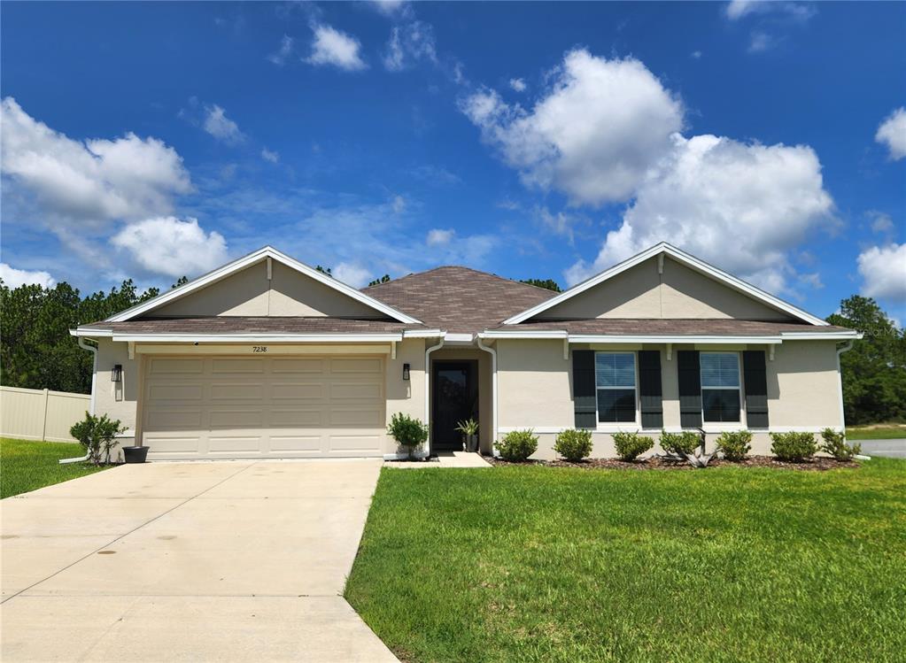 A single-story house with a beige stucco exterior, a two-car garage, and a front lawn — 7238 SW 136TH LANE, OCALA, FL