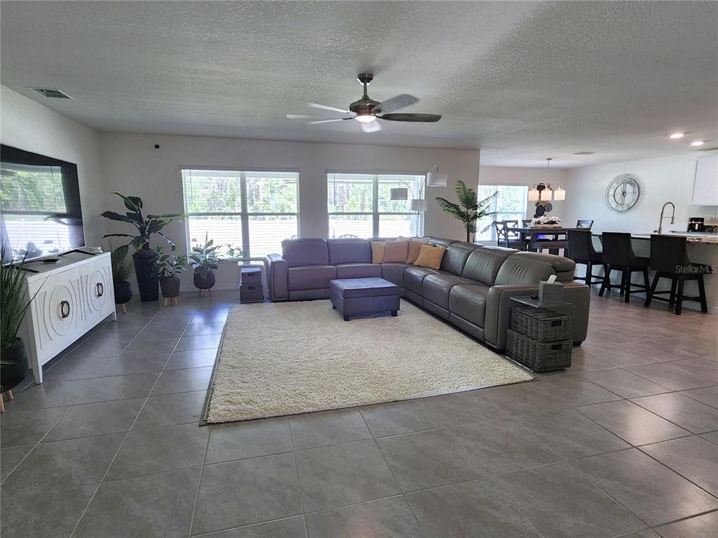 An open-concept living room features gray tile flooring, a large sectional sofa, and a kitchen — 7238 SW 136TH LANE, OCALA, FL
