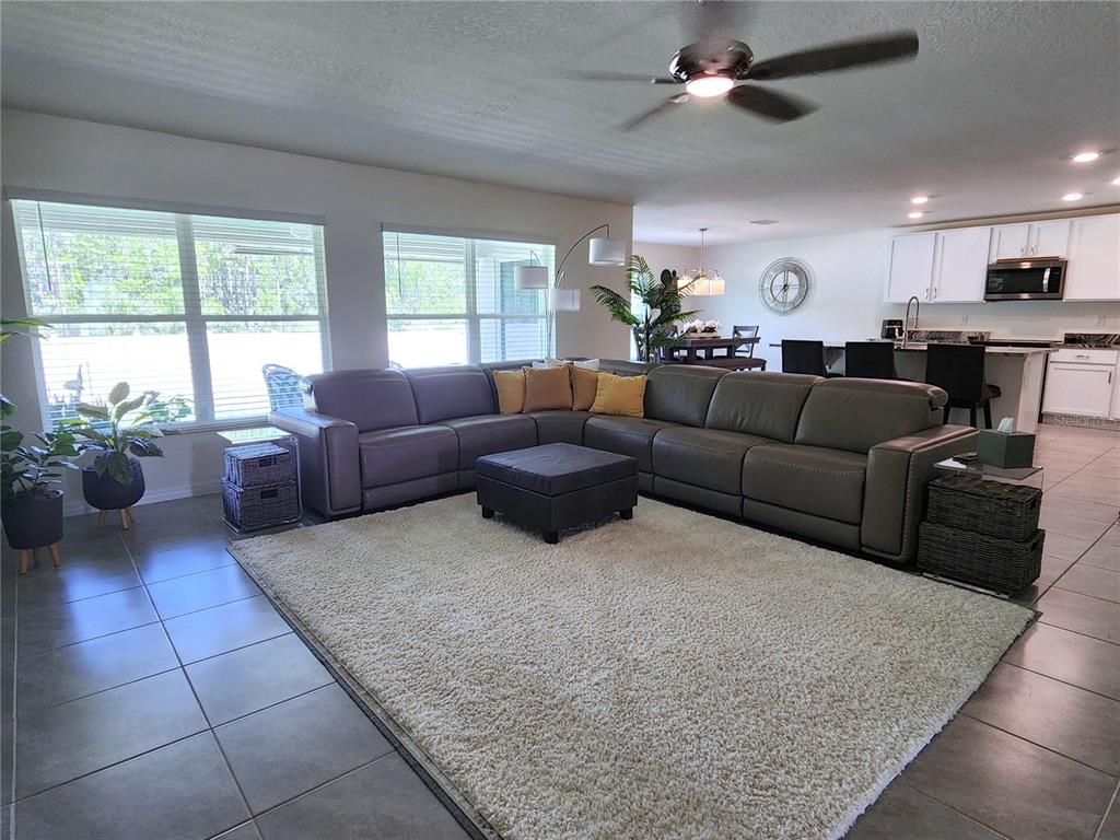 An open-concept living room features a large sectional sofa, a shag rug, and tile flooring — 7238 SW 136TH LANE, OCALA, FL