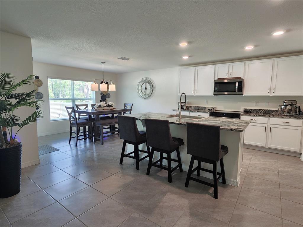 A kitchen with white cabinets and a granite island opens to a dining area — 7238 SW 136TH LANE, OCALA, FL
