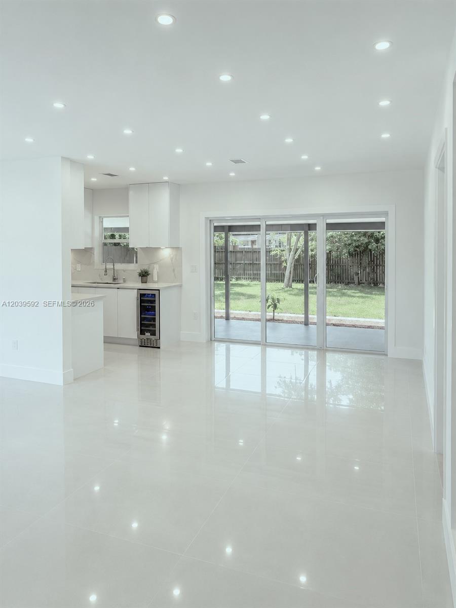 A bright, open-concept kitchen and living area features white cabinetry, glossy tile floors, and sliding glass doors — 18935 NW 8th Ave, Miami Gardens FL 33169, MIAMI GARDENS, FL