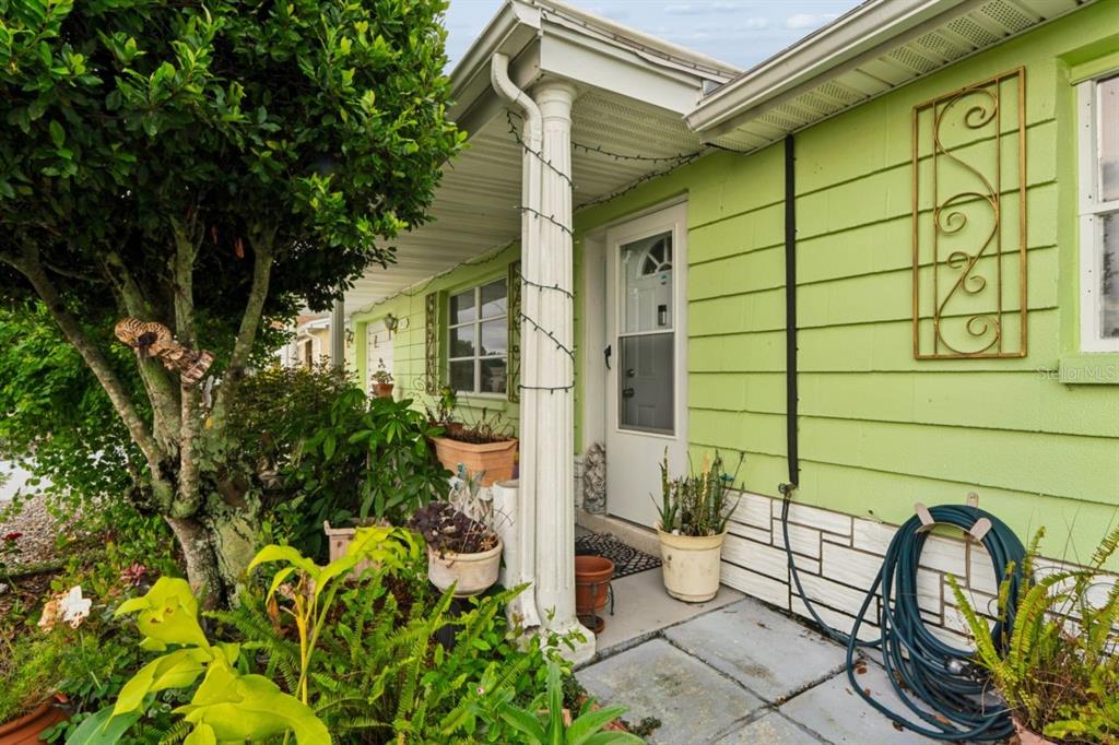 A lime green house exterior features a covered porch, a white door, and potted plants — 3415 CLYDESDALE DR unit 5, HOLIDAY, FL
