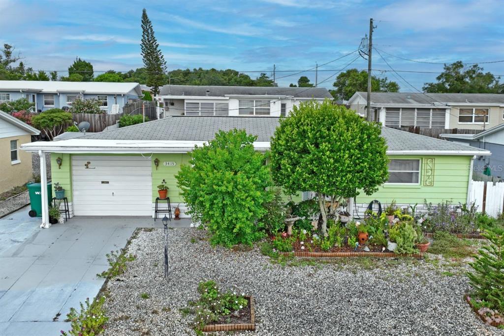 A light green single-story house features a gravel front yard, a garage, and mature landscaping — 3415 CLYDESDALE DR unit 5, HOLIDAY, FL