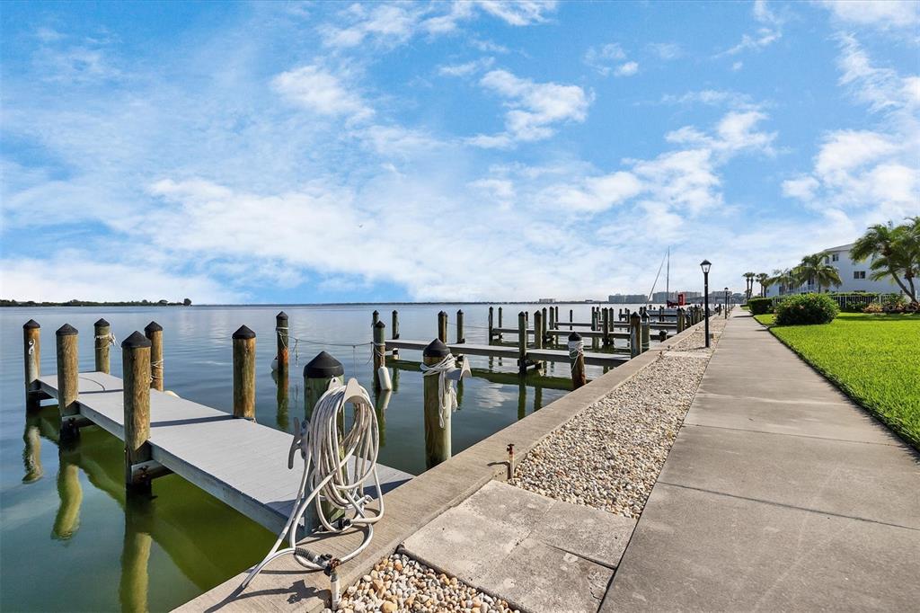A concrete walkway runs alongside a wooden boat dock extending into a calm bay — 769 JOHN RINGLING BOULEVARD UNIT 36EXET, SARASOTA, FL