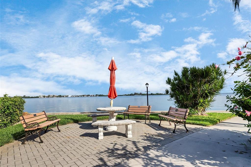A paved patio with a table, umbrella, and benches overlooks a calm body of water — 769 JOHN RINGLING BOULEVARD UNIT 36EXET, SARASOTA, FL