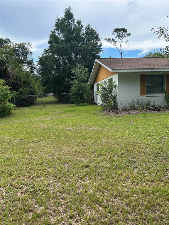 A side view of a white house with orange trim and a chain-link fence — 305 VIOLETWOOD ROAD, DELAND, FL