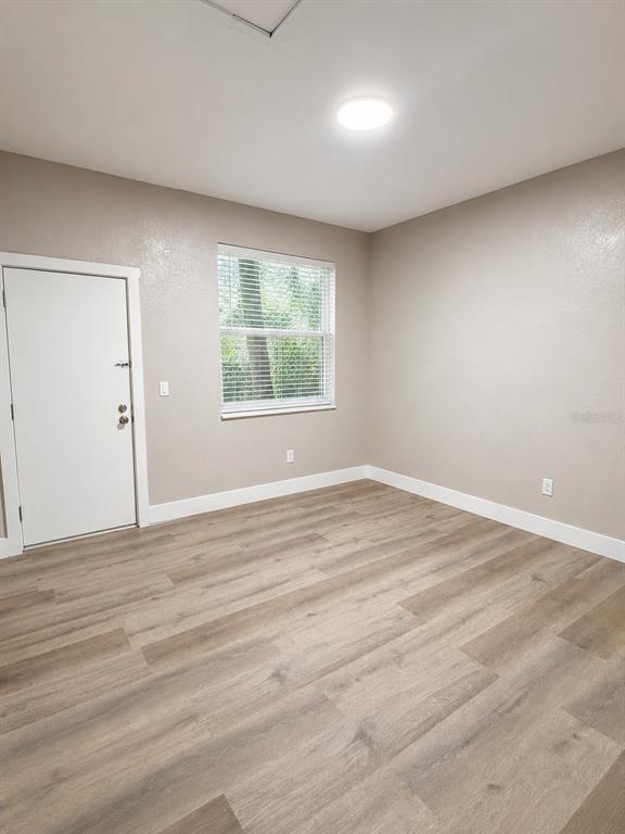 An empty room features light wood-look flooring, beige walls, a white door, and a window — 1244 23RD STREET, ORLANDO, FL