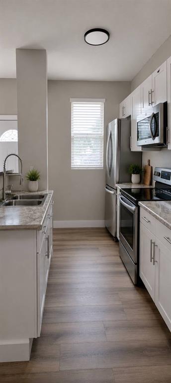 A narrow kitchen features white cabinets, stainless steel appliances, and light wood-look flooring — 1244 23RD STREET, ORLANDO, FL