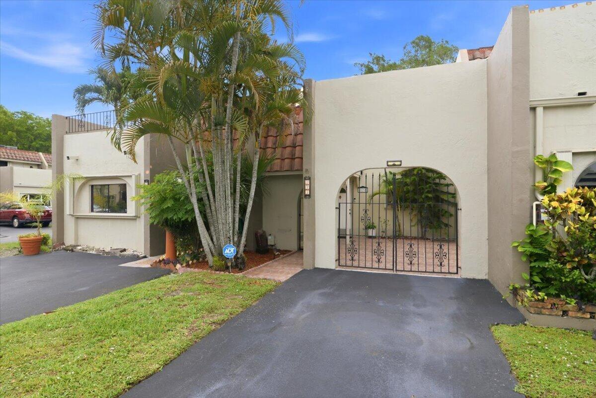 A tan stucco townhouse exterior features a gated courtyard entrance and a palm tree — 275 Jacaranda Drive, Plantation FL 33324, PLANTATION, FL