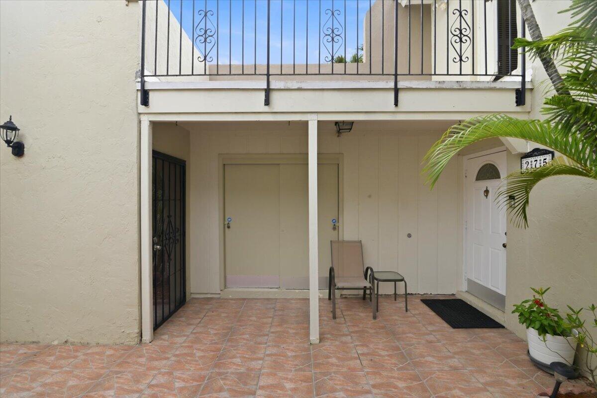 A tiled patio features a white front door, a metal chair, and a balcony above — 275 Jacaranda Drive, Plantation FL 33324, PLANTATION, FL