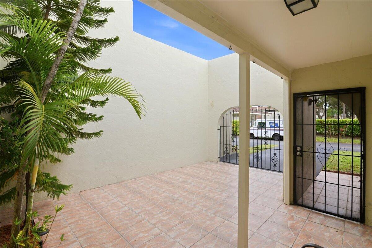 A tiled outdoor patio features a palm tree, a metal gate, and a covered entryway — 275 Jacaranda Drive, Plantation FL 33324, PLANTATION, FL