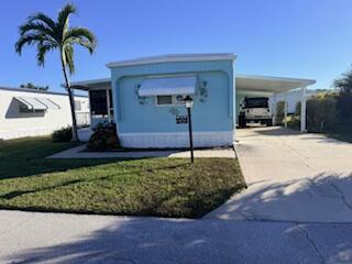 A light blue mobile home features a carport, a palm tree, and a small front lawn — 102 N Warner Drive, Jensen Beach FL 34957, JENSEN BEACH, FL