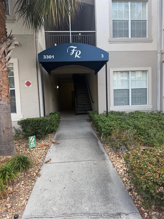 A concrete walkway leads to the covered entrance of a multi-story apartment building — 3301 WHITESTONE CIRCLE UNIT 205, KISSIMMEE, FL