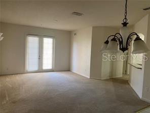 A carpeted living room features a chandelier, neutral walls, and glass doors leading outside — 3301 WHITESTONE CIRCLE UNIT 205, KISSIMMEE, FL