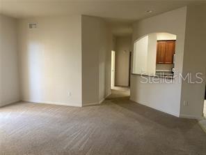 A carpeted living room opens to a kitchen with wooden cabinets and an arched pass-through — 3301 WHITESTONE CIRCLE UNIT 205, KISSIMMEE, FL