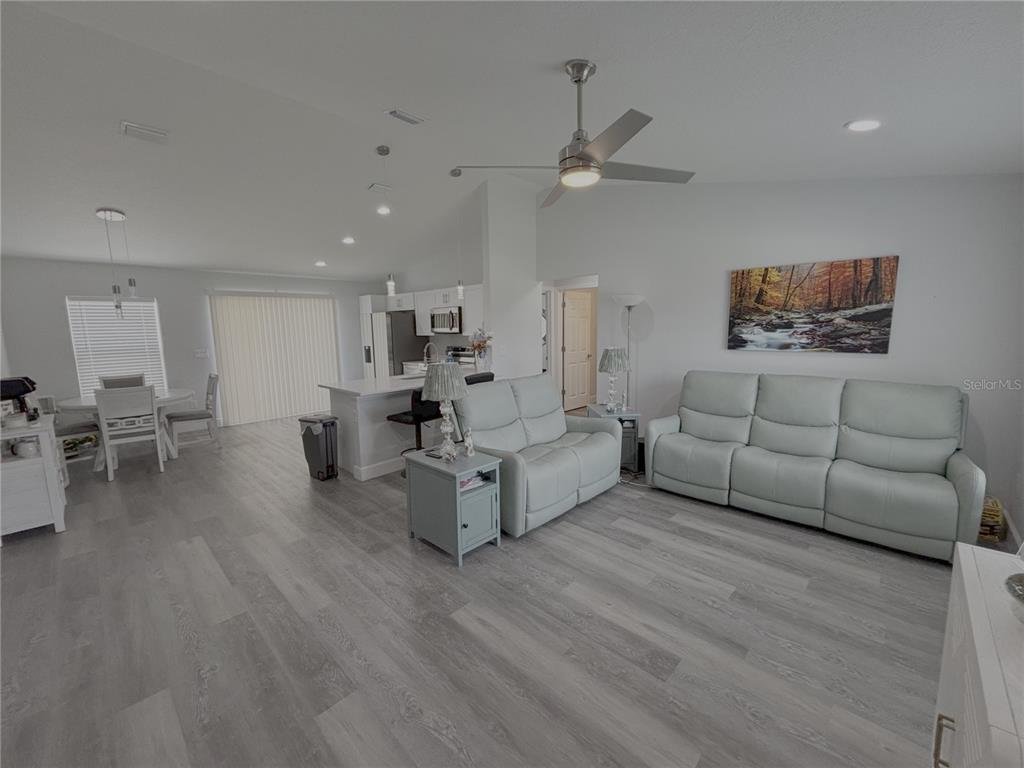 An open-concept living room and kitchen feature light gray flooring and white leather furniture — 3722 SW 149TH TERRACE, OCALA, FL