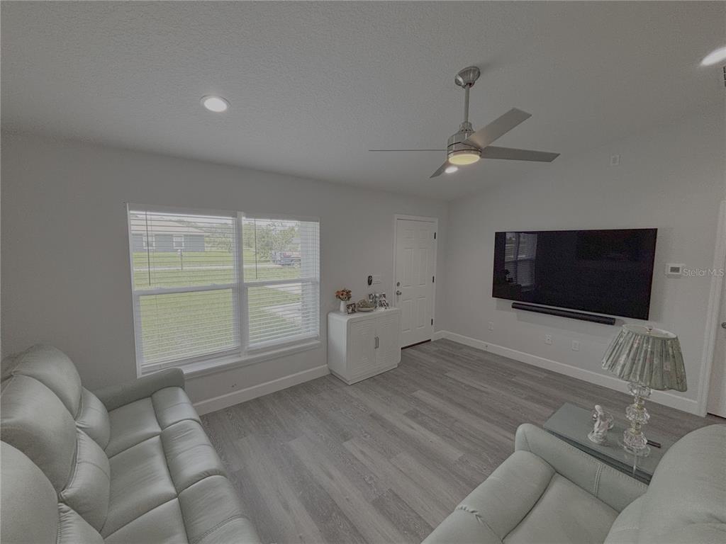 A living room features light gray flooring, a ceiling fan, and a wall-mounted television — 3722 SW 149TH TERRACE, OCALA, FL