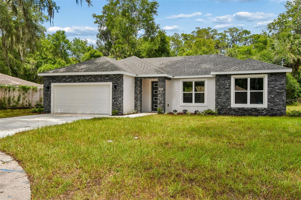 A single-story house with a white stucco facade, stone veneer accents, and a two-car garage — 3515 JERATHAN DRIVE, DELAND, FL