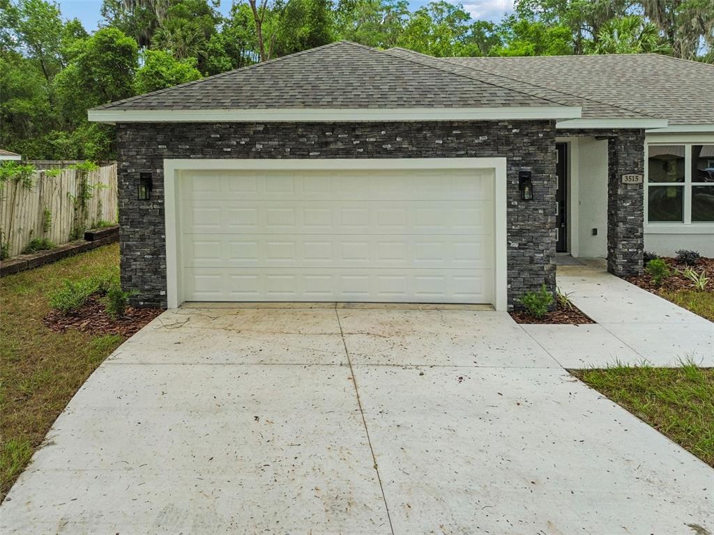 A single-story house exterior features a white garage door, stone veneer siding, and concrete driveway — 3515 JERATHAN DRIVE, DELAND, FL