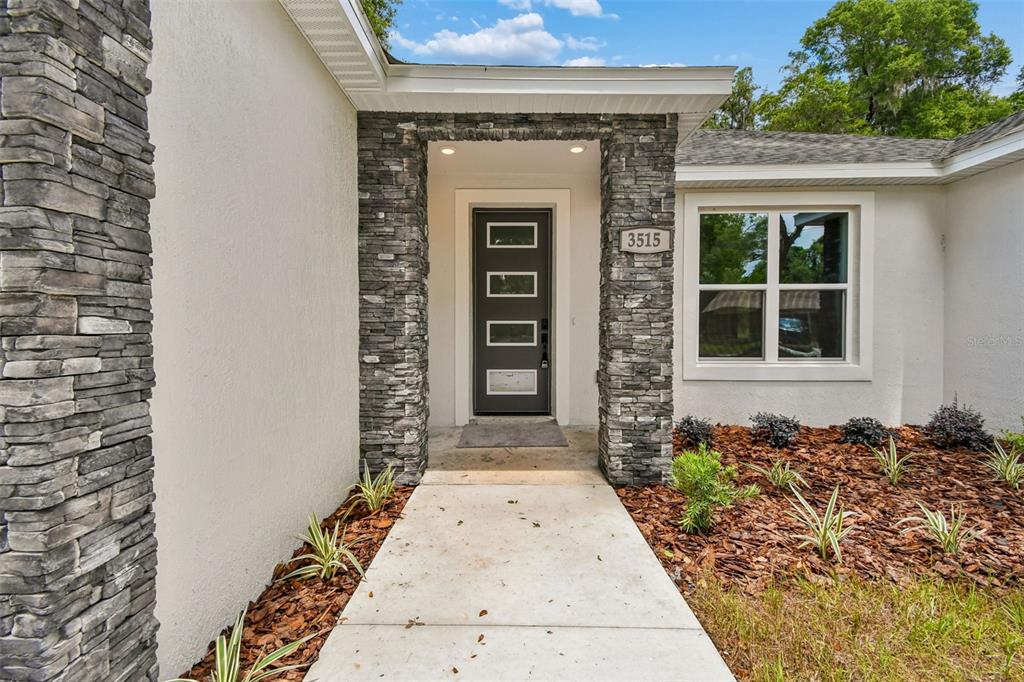 The front entrance features a dark door with four glass panels and stone-clad pillars — 3515 JERATHAN DRIVE, DELAND, FL