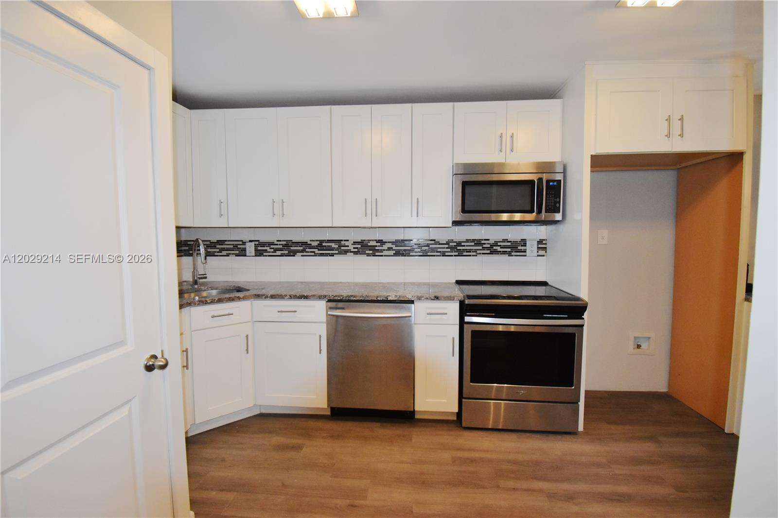 A kitchen features white cabinets, stainless steel appliances, granite countertops, and a tiled backsplash — 6080 NW 44th St # 201, Lauderhill FL 33319, LAUDERHILL, FL