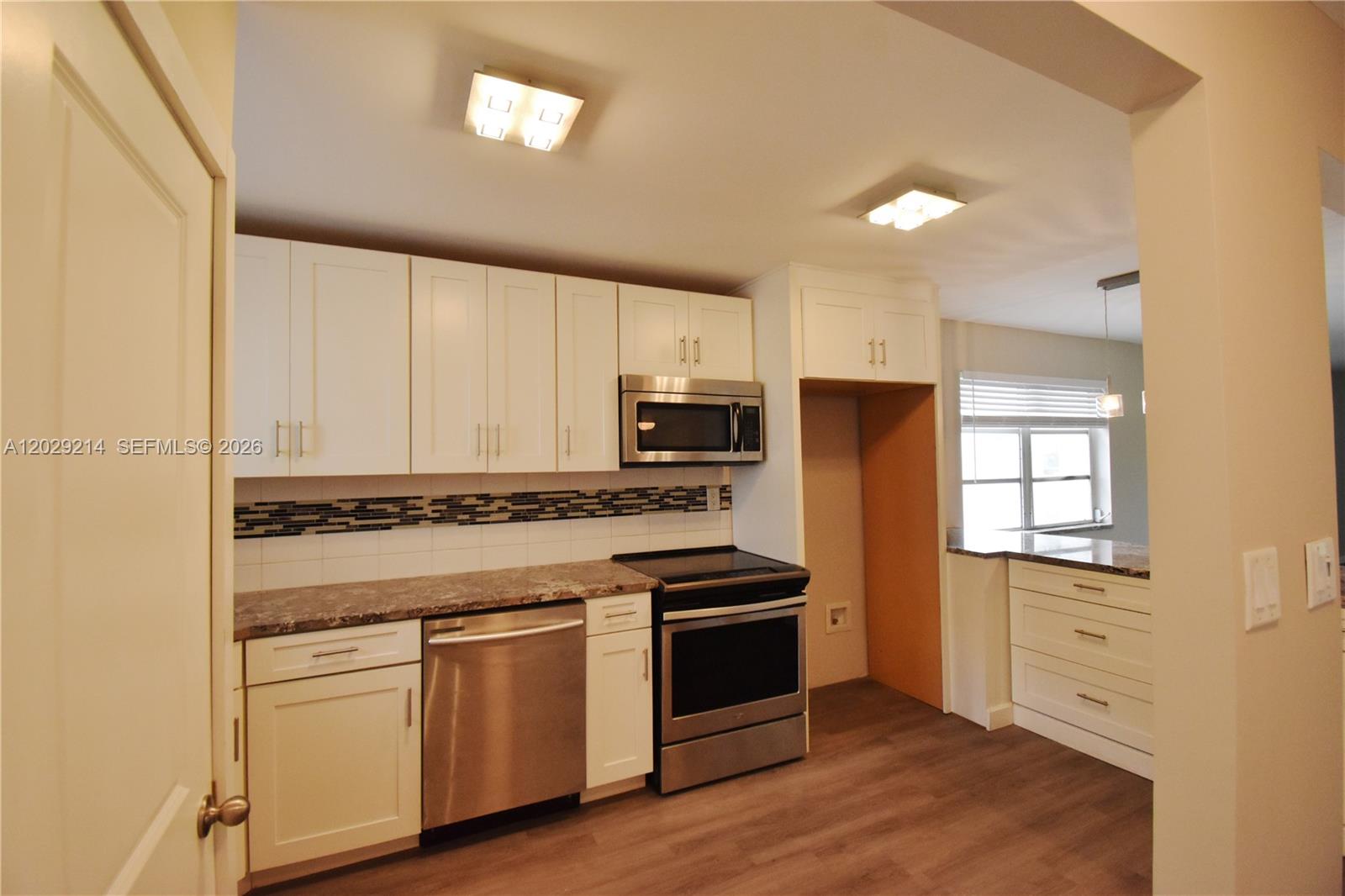A kitchen features white cabinets, stainless steel appliances, a tiled backsplash, and wood-look flooring — 6080 NW 44th St # 201, Lauderhill FL 33319, LAUDERHILL, FL