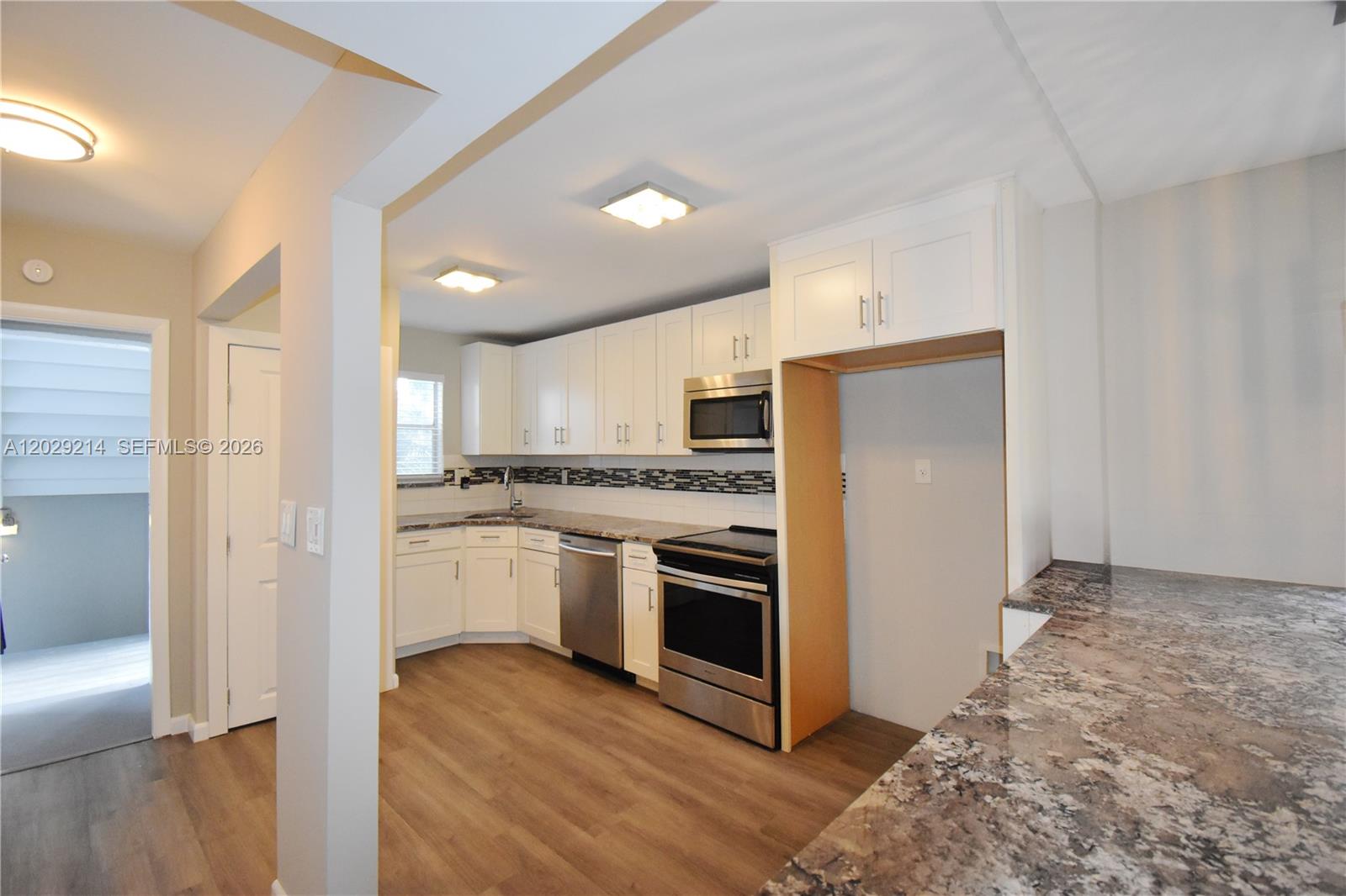 A kitchen features white cabinets, stainless steel appliances, and granite countertops with wood-look flooring — 6080 NW 44th St # 201, Lauderhill FL 33319, LAUDERHILL, FL