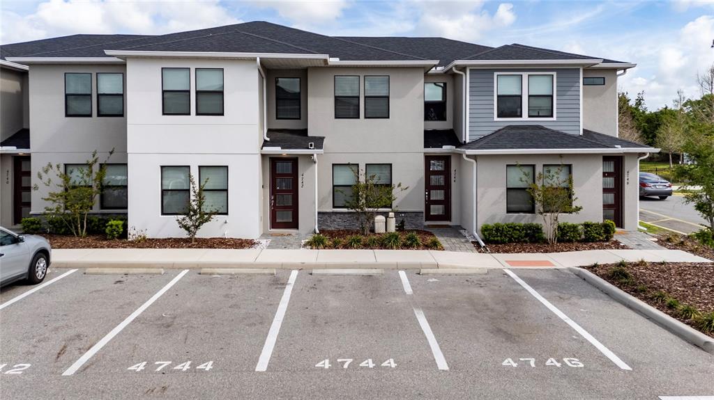 A multi-unit townhouse building features gray stucco siding, dark roofs, and assigned parking spaces — 4744 TERRA ESMERALDA DRIVE, KISSIMMEE, FL