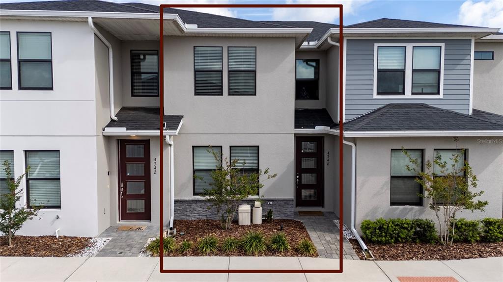 The exterior of a two-story townhouse features a gray stucco facade, stone accents, and dark-framed windows — 4744 TERRA ESMERALDA DRIVE, KISSIMMEE, FL