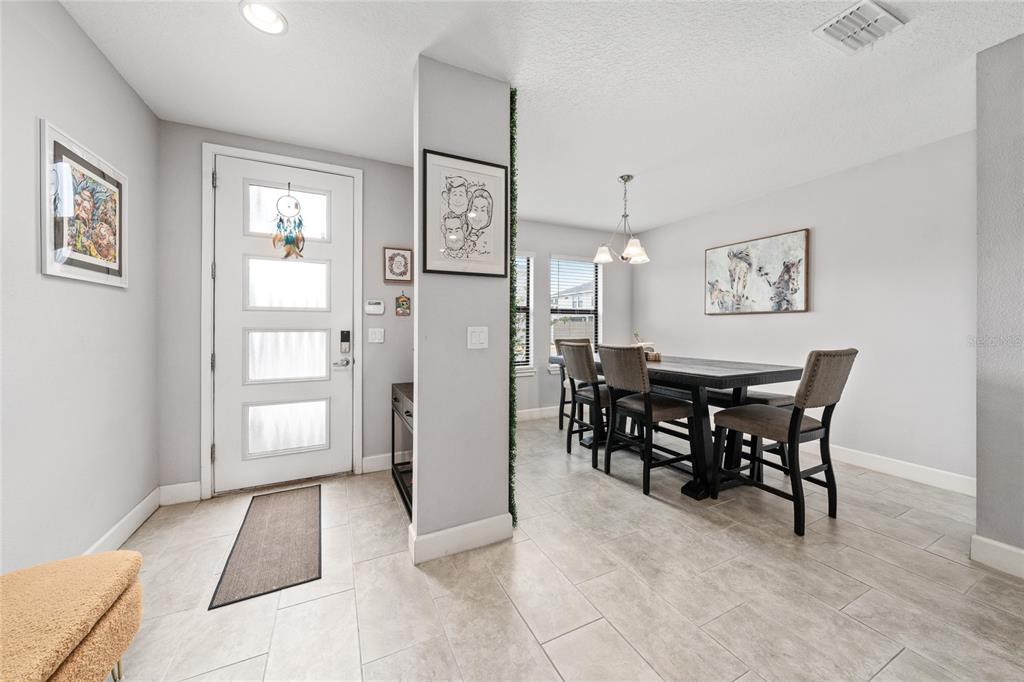 A dining area with a dark table and chairs sits adjacent to a white front door — 4744 TERRA ESMERALDA DRIVE, KISSIMMEE, FL