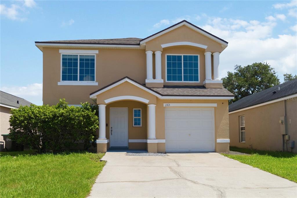 A two-story tan stucco house features a front porch with columns and a garage — 1365 CAREY GLEN CIRCLE, ORLANDO, FL