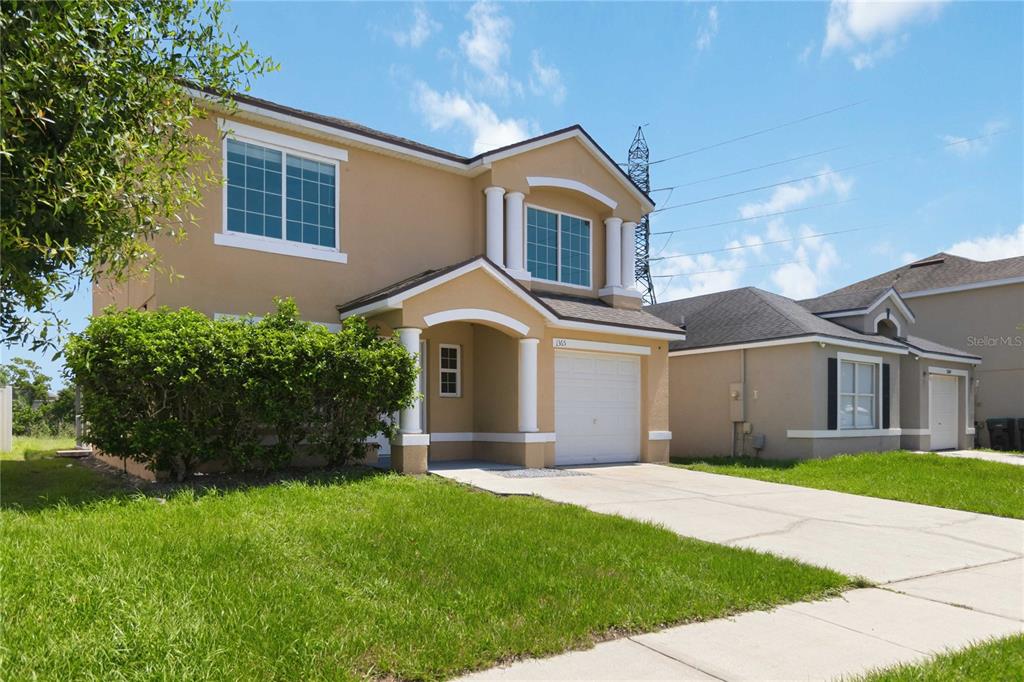 A two-story tan house with a white garage and a front porch under a blue sky — 1365 CAREY GLEN CIRCLE, ORLANDO, FL