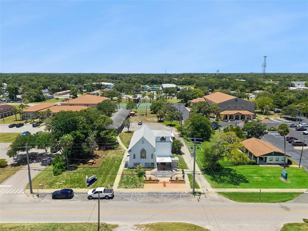 An aerial view shows a white church building surrounded by trees, parking lots, and roads — 1050 DAYTONA AVENUE, DAYTONA BEACH, FL