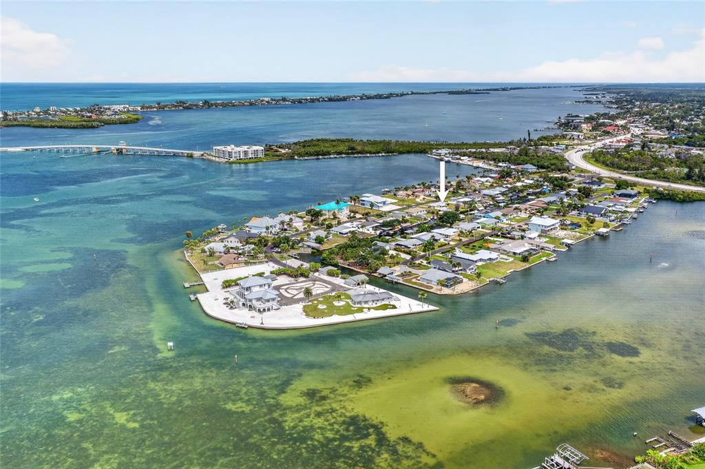 An aerial view shows a coastal residential neighborhood surrounded by water with a white arrow — 1447 LEMON BAY DRIVE, ENGLEWOOD, FL