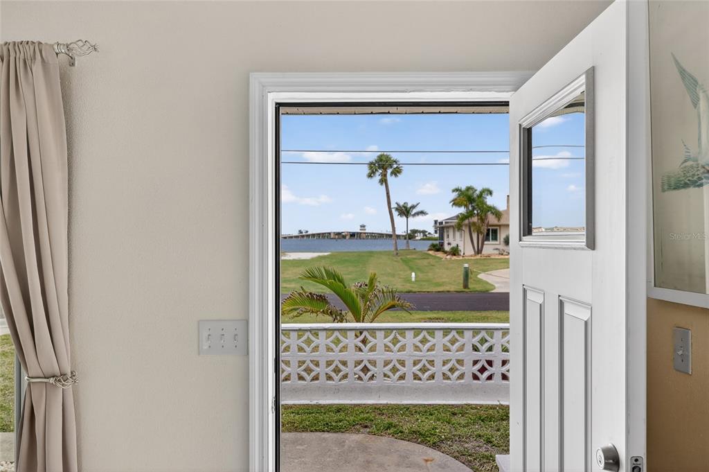An open white door reveals a view of a lawn, palm trees, and a bridge — 1447 LEMON BAY DRIVE, ENGLEWOOD, FL