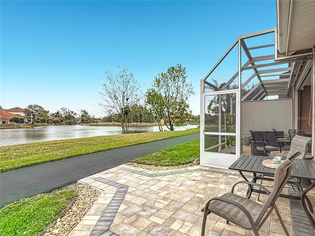 A paved patio with outdoor furniture sits beside a screened enclosure overlooking a lake — 6828 SOMBRAS WAY, LAND O LAKES, FL
