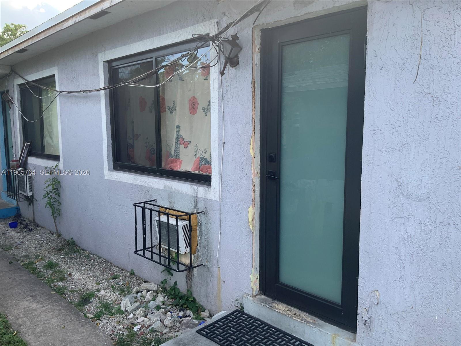 The exterior of a house features a frosted glass door, a window, and a wall-mounted AC — 896 NW 103rd St, Miami FL 33150, MIAMI, FL