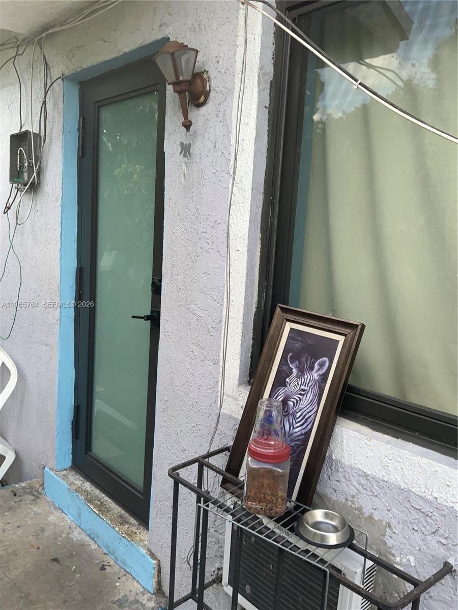 An exterior view shows a door, a window, a wall-mounted light, and a metal rack with a picture — 896 NW 103rd St, Miami FL 33150, MIAMI, FL