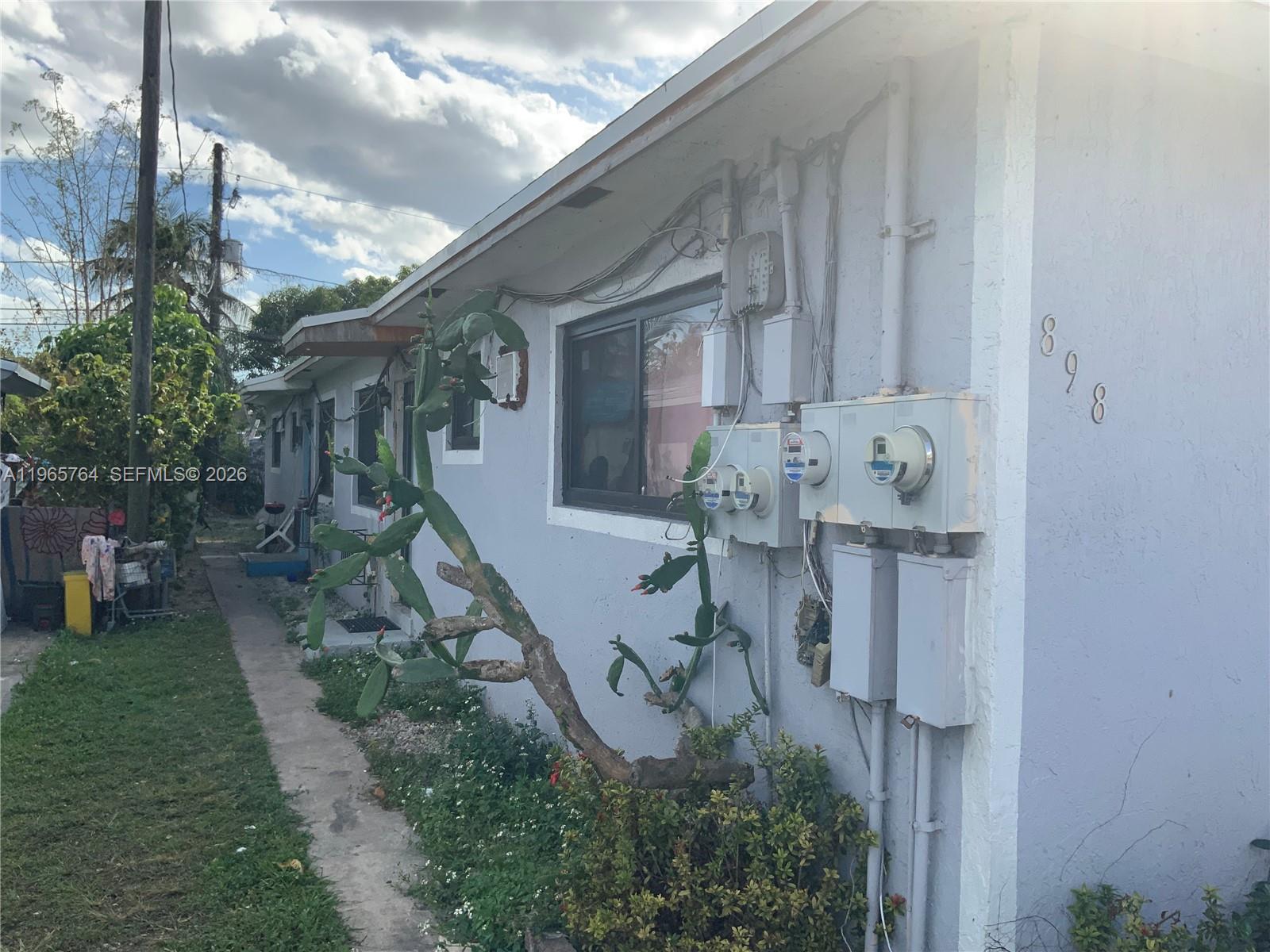 The exterior of a light-colored house features a cactus, utility meters, and a walkway — 896 NW 103rd St, Miami FL 33150, MIAMI, FL