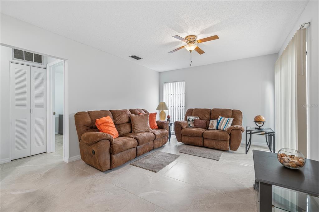 A living room features two brown reclining sofas, tile flooring, and a ceiling fan — 10307 PENNYTREE PLACE, TAMPA, FL