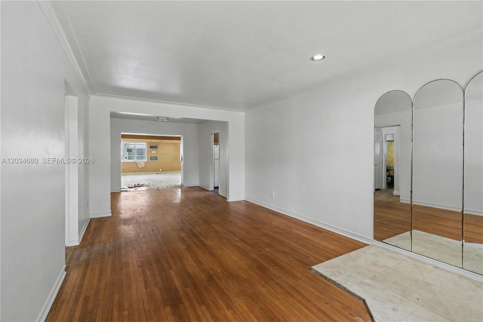 An empty room features hardwood floors, white walls, and a large arched mirror panel — 236 Candia Ave, Coral Gables FL 33134, CORAL GABLES, FL
