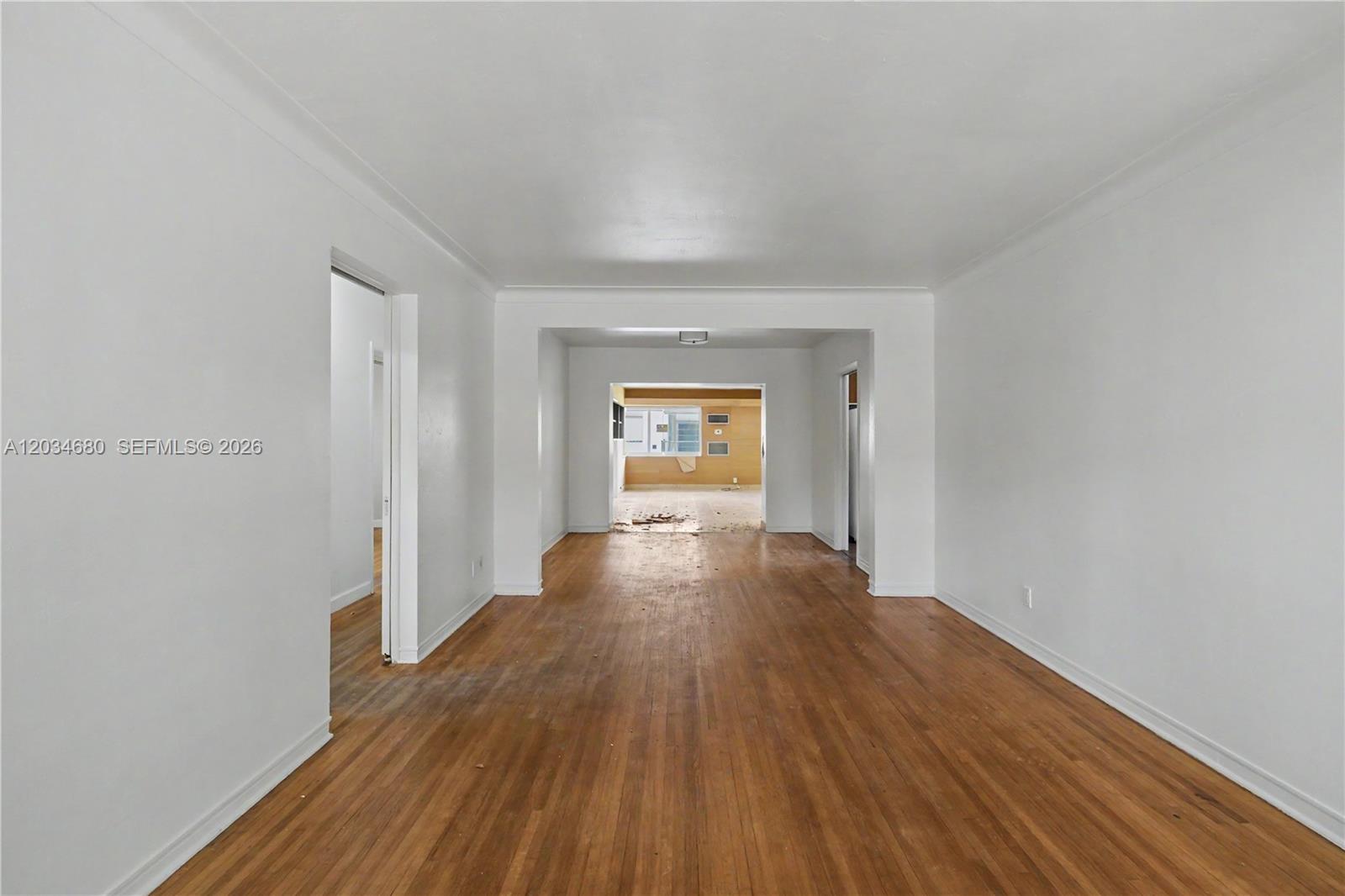 An empty room with hardwood floors leads into a second room with a window — 236 Candia Ave, Coral Gables FL 33134, CORAL GABLES, FL