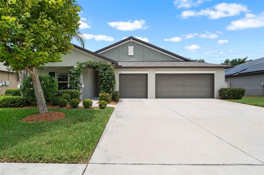 A single-story house features a three-car garage, a concrete driveway, and a landscaped front yard — 809 TIMELESS MOSS DRIVE, RUSKIN, FL