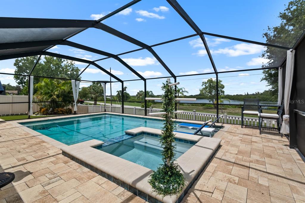 A screened-in pool and spa area features stone pavers and a view of a lake — 809 TIMELESS MOSS DRIVE, RUSKIN, FL
