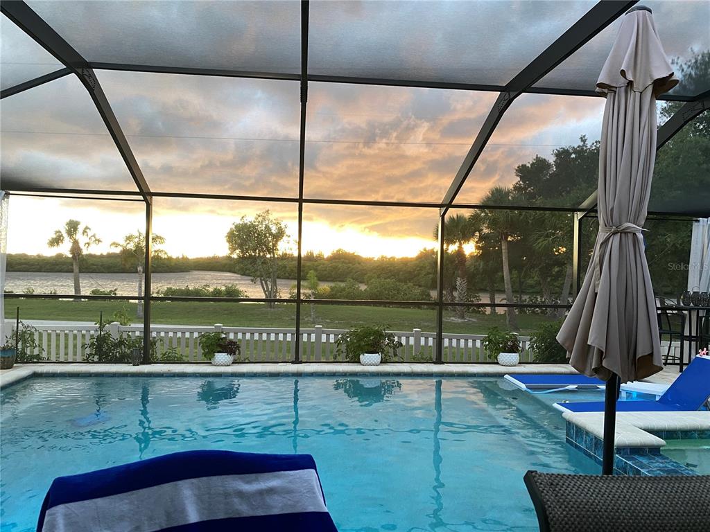 A swimming pool with a screened-in lanai overlooks a grassy yard and a body of water — 809 TIMELESS MOSS DRIVE, RUSKIN, FL