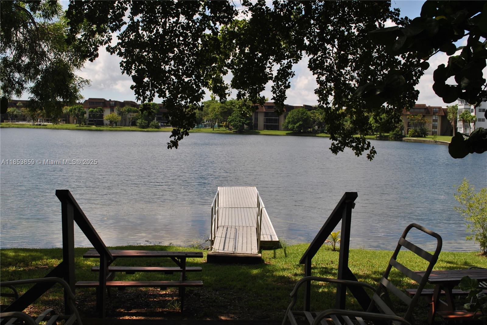 A wooden dock extends into a lake from a grassy lawn with outdoor seating — 19941 NE 5th Ct # 3M, Miami FL 33179, MIAMI, FL